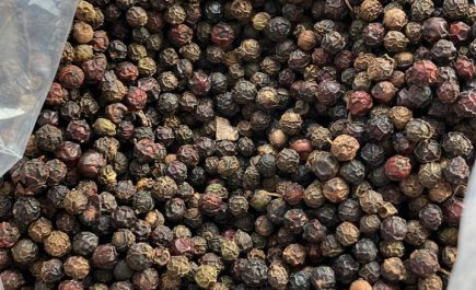 A close-up photo of shiny black peppercorns, showcasing their deep, rich color and textured surface, piled loosely on a rustic wooden background, highlighting the natural and organic essence of the spice.